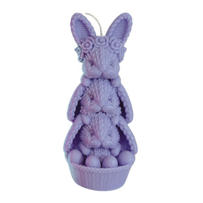A lavender purple Easter-themed candle shaped like a bunny sitting in a basket with eggs, featuring textured knit details and a small wick at the top